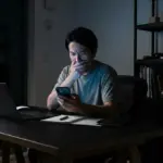 A concerned banking customer looking at a phone screen in a dark room.